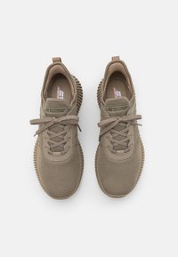 Baskets en maille beige avec des lacets ronds, des semelles en caoutchouc texturé et un design épuré ; portant la marque "SKECHERS" sur les côtés.