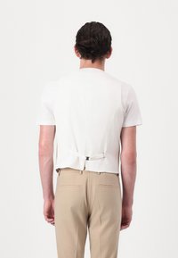 Camicia bianca a maniche corte, con schiena strutturata e cinturino regolabile, abbinata a pantaloni beige chiaro con due tasche posteriori.