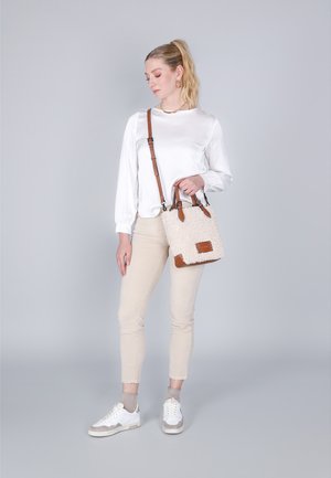 Beige tote taske med en tekstureret, fluffy overflade og brune læderdetaljer. Justerbar rem og dobbelt top-håndtag. Båret med lyse bukser og sneakers.