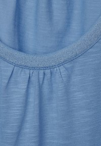 Light blue fabric with a textured finish, featuring a gathered seam and a smooth, contrasting round neckline. Subtle sheen in stitching.