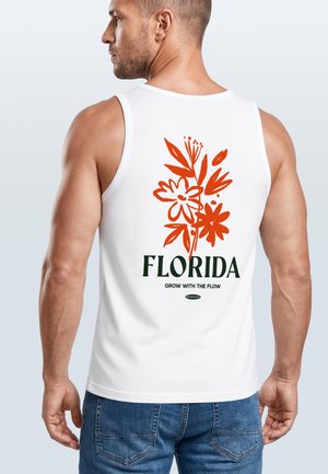 Man wearing white tank top with orange floral design and text "Florida Grow with the Flow" on back, paired with blue jeans.