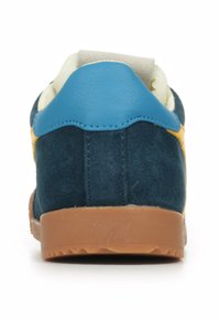 Zapatilla de gamuza azul con un acento amarillo, que cuenta con una suela de goma y un cuello acolchado. Textura suave con elementos contrastantes en la parte posterior.