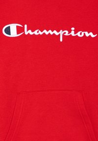 Sudadera roja fabricada en una mezcla de algodón, que presenta un gran logo bordado en blanco de "Champion" en el pecho y un bolsillo tipo canguro en la parte delantera.