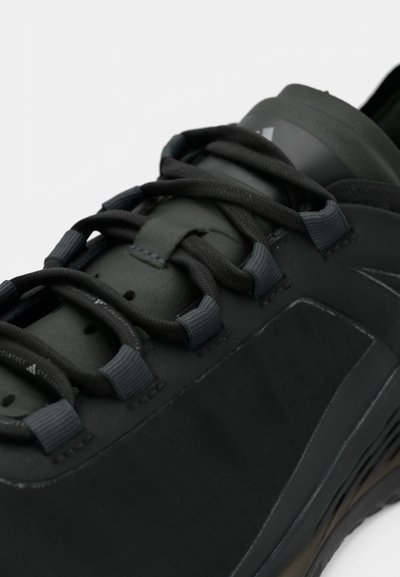 Μαύρο αθλητικό παπούτσι με υφή στην επάνω επιφάνεια, ενισχυμένο σύστημα κορδονιών και διαμορφωμένη φτέρνα. Λεπτομέρειες από λείο ύφασμα και σόλα από καουτσούκ.