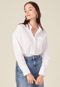 Witte overhemd met een enkele borstzak, gecombineerd met een hooggeprijsde blauwe spijkerrok. Het shirt heeft lange mouwen en een kraag.