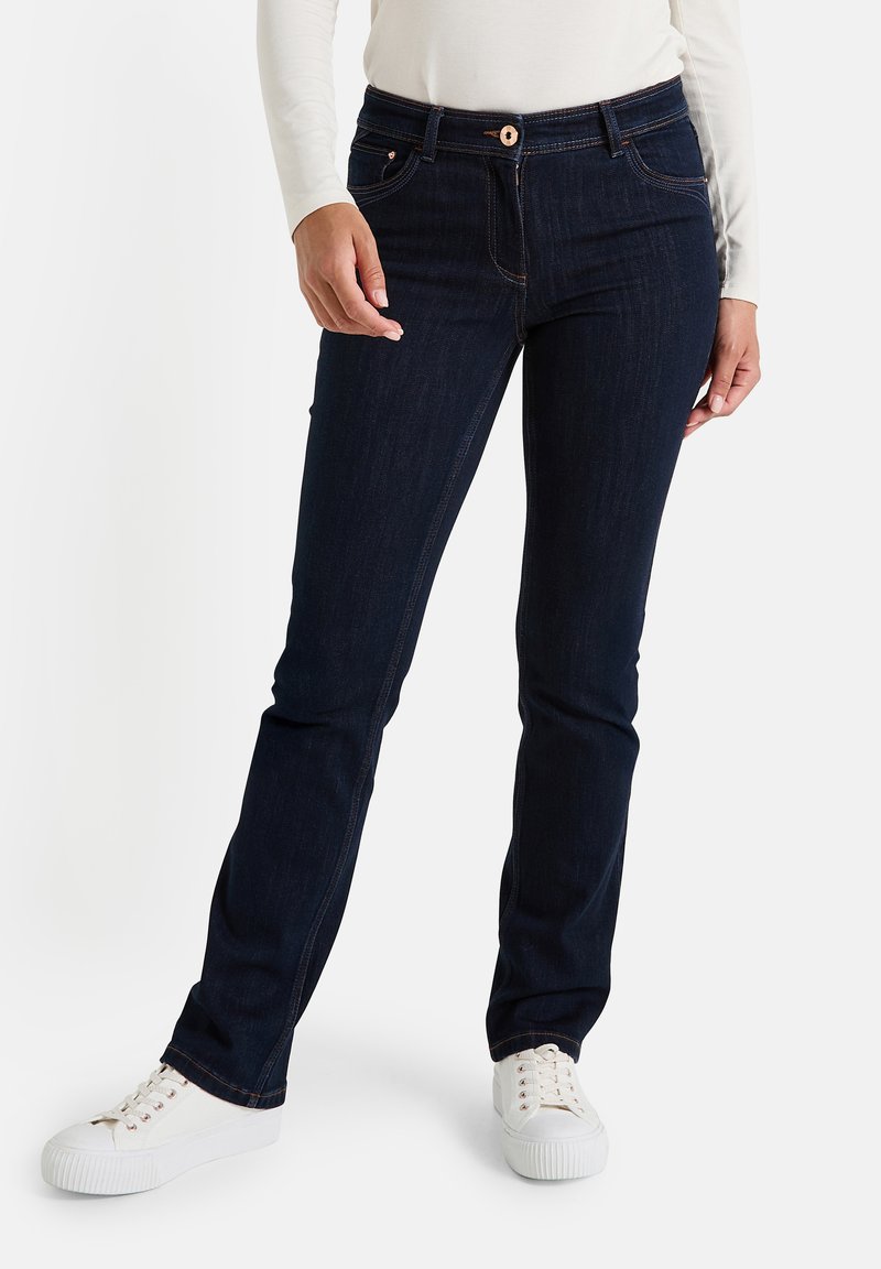 Jeans de denim oscuro con corte recto, que cuentan con cierre de botón, cinco bolsillos y costuras en contraste, combinados con zapatillas blancas.