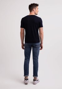 Marinblå kortärmad skjorta, figurnära design, tillverkad av bomullsmaterial. Bärs med uppvikta ärmar, ljusblå denimjeans och vita sneakers med svarta detaljer.