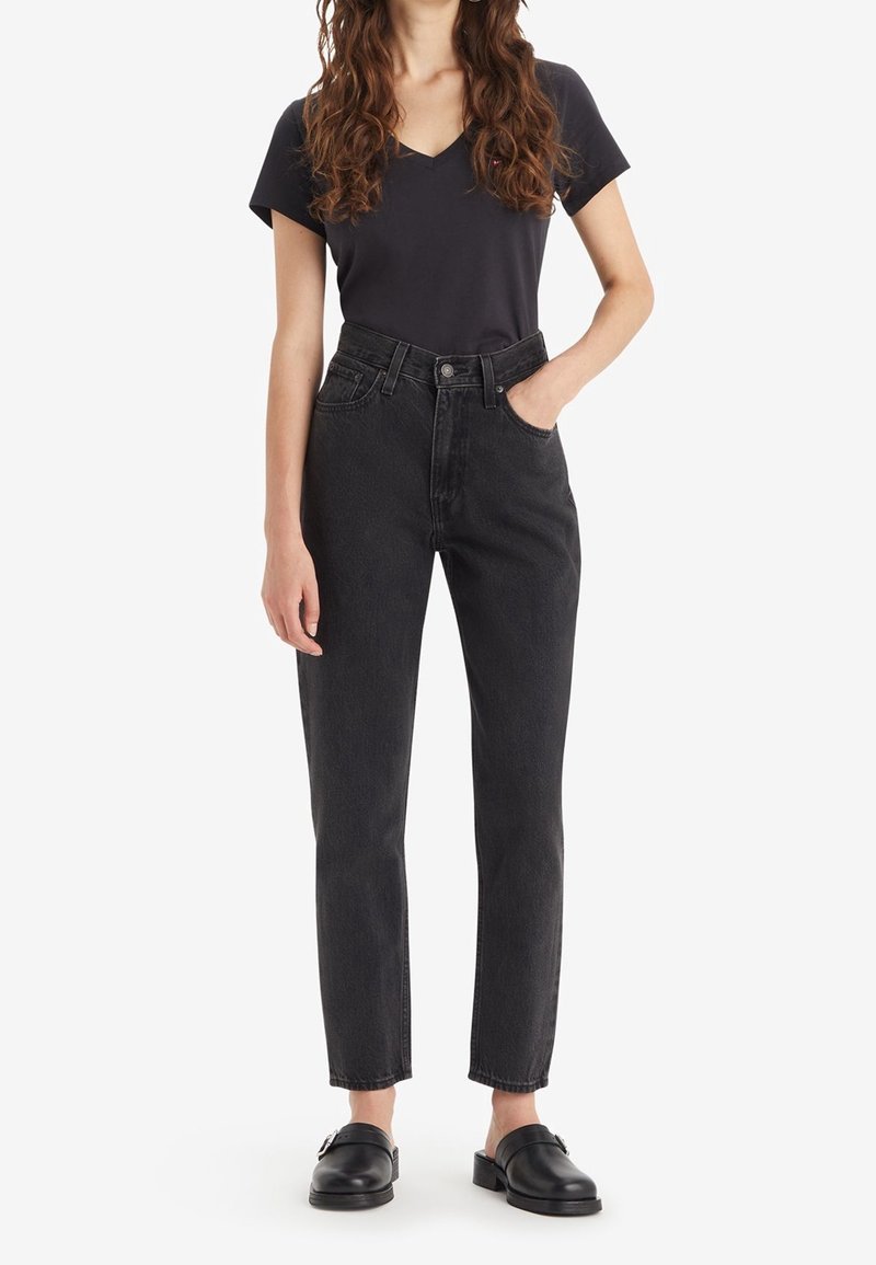 Svarta högmidjade jeans med rak benklippning, femficksdesign och klassisk knappgylf, tillsammans med en mörk t-shirt med v-ringning.