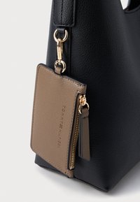 Sort struktureret lædertaske med en tan farvet lynlåset kortholder vedhæftet. Guldhardware og et strømlinet design.