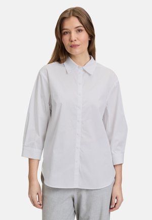 White, button-up shirt with a collar, three-quarter sleeves, and a smooth texture. Paired with light gray trousers, minimal details.