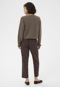 Brown knitted sweater with a cropped design, paired with dark brown straight-leg pants. Soft texture and relaxed fit throughout.
