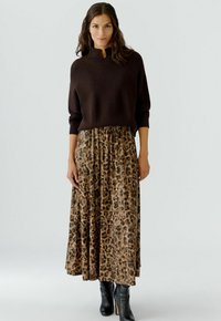 Bruin gebreid sweater met hoge hals, gecombineerd met een leeuwenprint, vloeiende maxi rok. Model draagt zwarte hakschoenen.