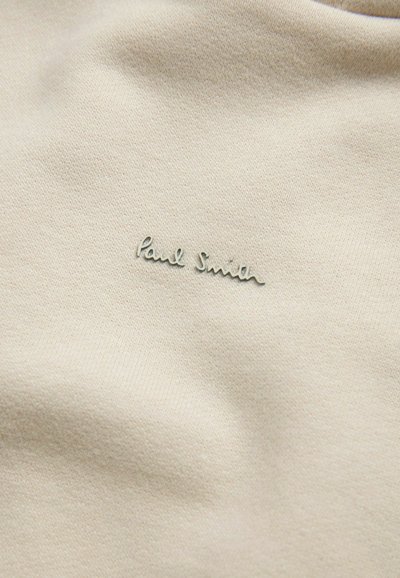 Tessuto di cotone beige con una trama sottile e il logo ricamato "Paul Smith" in turchese chiaro. Nessun motivo o accento aggiuntivo presente.