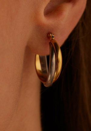 Gros plan d'une oreille avec une boucle d'oreille anneau bicolore présentant des bandes entrelacées d'or et d'argent.