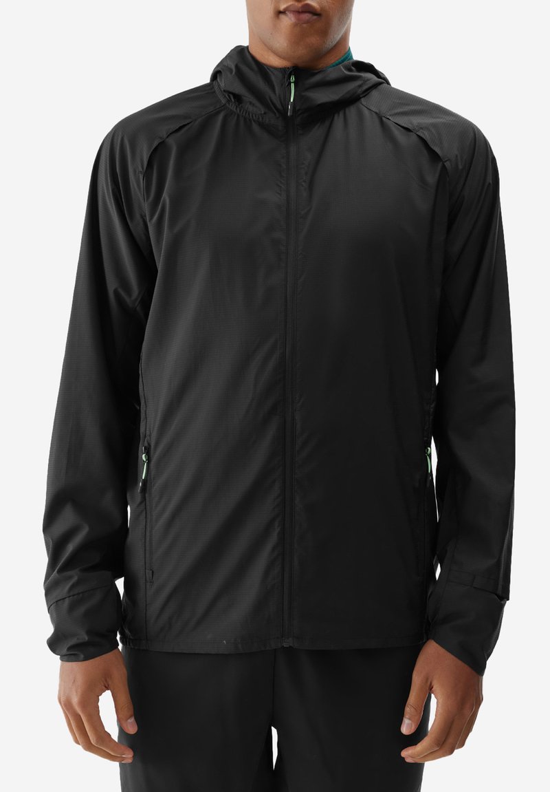 Czarna, lekka kurtka z kapturem, zapinana na zamek z przodu i z kieszeniami po bokach. Gładka faktura, minimalna ilość szwów oraz kontrastujące zielone akcenty zamka.