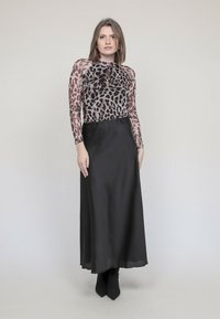 Haut à manches longues en imprimé léopard avec un tissu transparent ; associé à une jupe maxi en satin noir. Modèle portant des bottes à talons aiguilles noires.