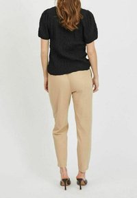 Blusa nera con texture e maniche a sbuffo, abbinata a pantaloni beige su misura e décolleté neri, vista da dietro.
