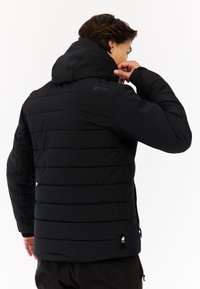 Zwarte gewatteerde jas met capuchon, met horizontale stiksels, elastische manchetten en een klein logo op de schouder, gemaakt van waterafstotend materiaal.