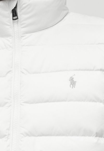 Λευκό μπουφάν puffer με όρθιο γιακά, διαθέτοντας καπιτονέ σχέδιο και γκρι κεντητό λογότυπο στο στήθος. Κλείσιμο με φερμουάρ.