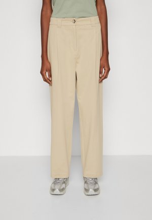 Beige straight-leg trousers with a button closure, flat front, and side pockets. Smooth texture and minimal design, paired with silver sneakers.