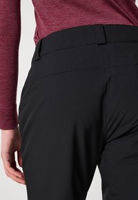 Zwarte op maat gemaakte broek met een gladde textuur en een aansluitende taille, gecombineerd met een bordeauxrode top met lange mouwen die een subtiel gebreid patroon vertoont.