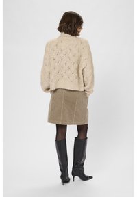 Grobstrick-beige Pullover mit einem strukturierten Muster, kombiniert mit einem beigen Cordrock und kniehohen schwarzen Lederstiefeln.
