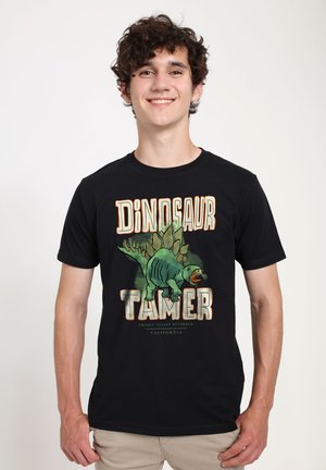 Maglietta nera con una grafica colorata di un dinosauro e la scritta "Domatore di Dinosauri". Progettata per un abbigliamento casual con maniche corte.