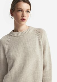 Ljus beige stickad tröja med rund ribbad halsringning, raglanärmar och ett texturerat mönster, utrustad med mjukt, tjockt garn.