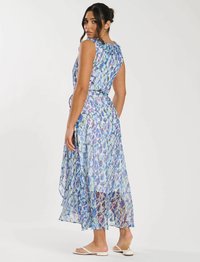 Leichtes, fließendes Maxikleid in Blau mit lila Blumenmustern, ärmelloses Design und gestuftem Saum, getragen mit flachen Sandalen.