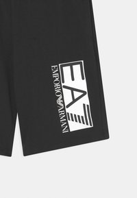 Černé šortky s velkým bílým potiskem, který zahrnuje "EA" a "Emporio Armani" s pruhovanými akcenty. Vyrobeno z hladkého, lehkého materiálu.