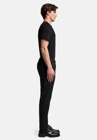 Maglietta nera a maniche corte abbinata a pantaloni neri slim-fit e scarpe nere. Tessuto morbido, design classico e silhouette aderente.