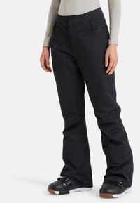 Zwarte sneeuwbroeken met een relaxte pasvorm, voorzien van een hoge tailleband, dubbele knopen en ruime zakken. Glad materiaal met een subtiele glans.