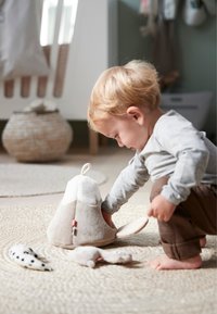 Knuffelopbergdoos in de vorm van een konijn, met zachte beige stof, grote slappe oren, roze accenten en een afgerond ontwerp. Kind speelt er vlakbij.