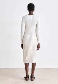 Kermainen ribbed midi-mekko pitkillä hihoilla, pukeutuva siluetti ja pyöreä pääntie. Tasainen, teksturoitu kangas, jossa on pystysuoria viivoja ja takasauma.