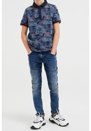 Granatowa koszulka polo z tropikalnym wzorem liści, pomarańczowe akcenty, w połączeniu z niebieskimi dżinsami i czarno-białymi trampkami.