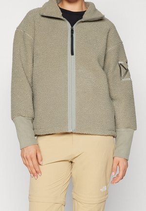Chaqueta de forro polar en verde oliva apagado con cremallera completa, cuello alto y puños grises en contraste. Presenta un parche lateral con detalle del logo.