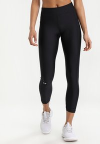 Czarne legginsy sportowe z elastycznego materiału, z wysokim stanem i dopasowanym krojem, w zestawieniu z białymi butami sportowymi.