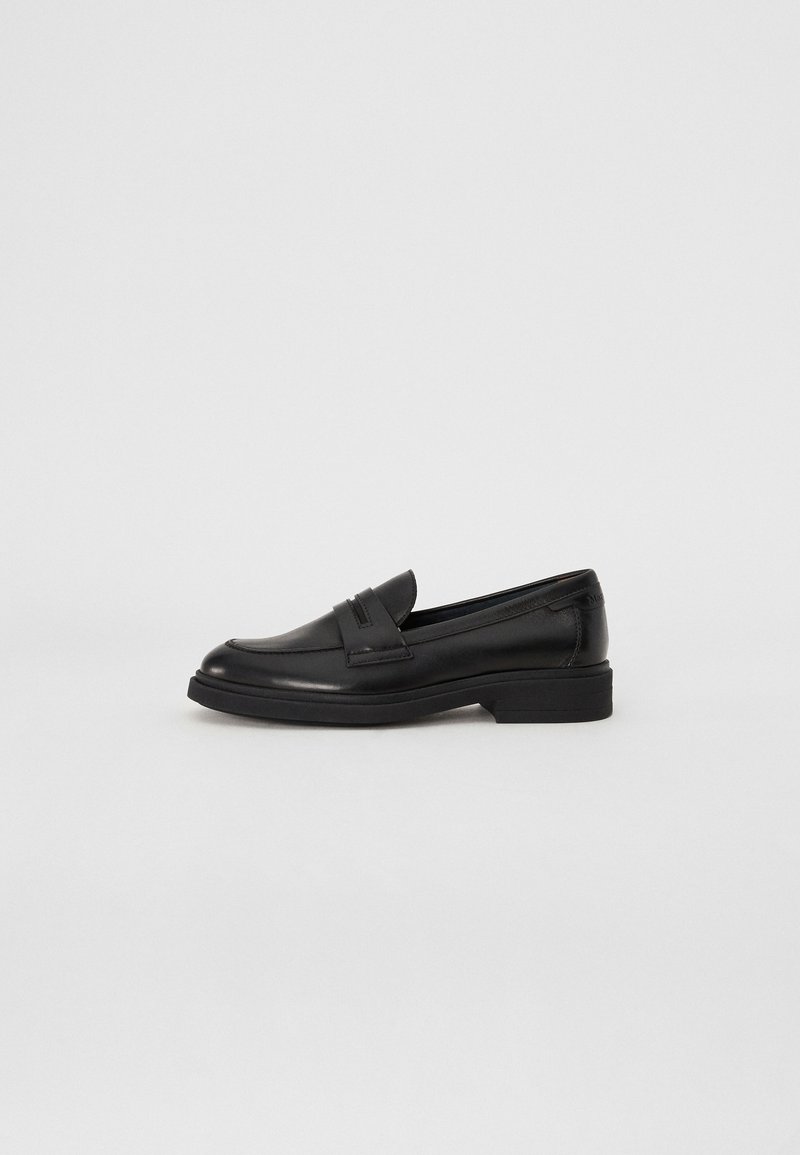 Mocassin en cuir noir avec un petit talon, un bout arrondi et un détail classique de bride à pampille, présenté en profil sur un fond uni.