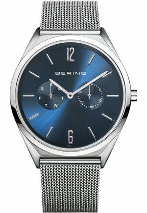 Montre Bering avec un bracelet en maille d'acier inoxydable, un cadran dégradé bleu, des index argentés, et deux sous-cadrans pour le jour et l'heure au format 24 heures.