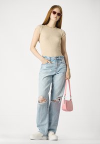 Haut beige à manches courtes en côtes, jeans large taille bleue clair avec de grandes déchirures, baskets blanches et un petit sac à main rose.