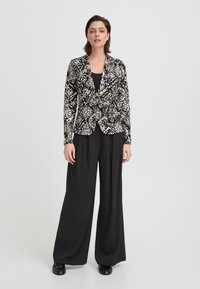 Blazer à motifs noir et blanc avec une coupe ajustée, doté d'un revers cranté et de manches longues, associé à un pantalon noir à jambes larges.