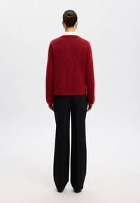 Suéter rojo de punto con un corte relajado, que presenta mangas largas y un cuello redondeado. Combinado con pantalones negros de tiro alto.