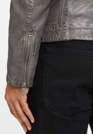 Graue Lederjacke mit strukturierter Oberfläche, silbernem Reißverschlussdetail am Ärmel, kombiniert mit schwarzen Jeanshosen mit herzförmiger Taschenstickerei.