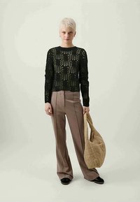 Sweater preto de malha de manga longa com um padrão floral, combinado com calças bejes de boca de sino e uma bolsa de ombro beje acolchoada. Sapatos pretos.