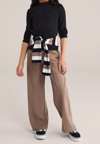 Top negro de manga larga con textura acanalada, combinado con pantalones beige de pierna ancha. Un pañuelo a rayas en tonos marrón, blanco y negro atado a la cintura.