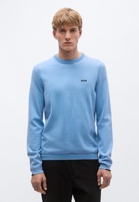 Világoskék környakú pulóver puha kötött anyagból, hosszú ujjakkal és a mellkason egy kis fekete "BOSS" logóval.