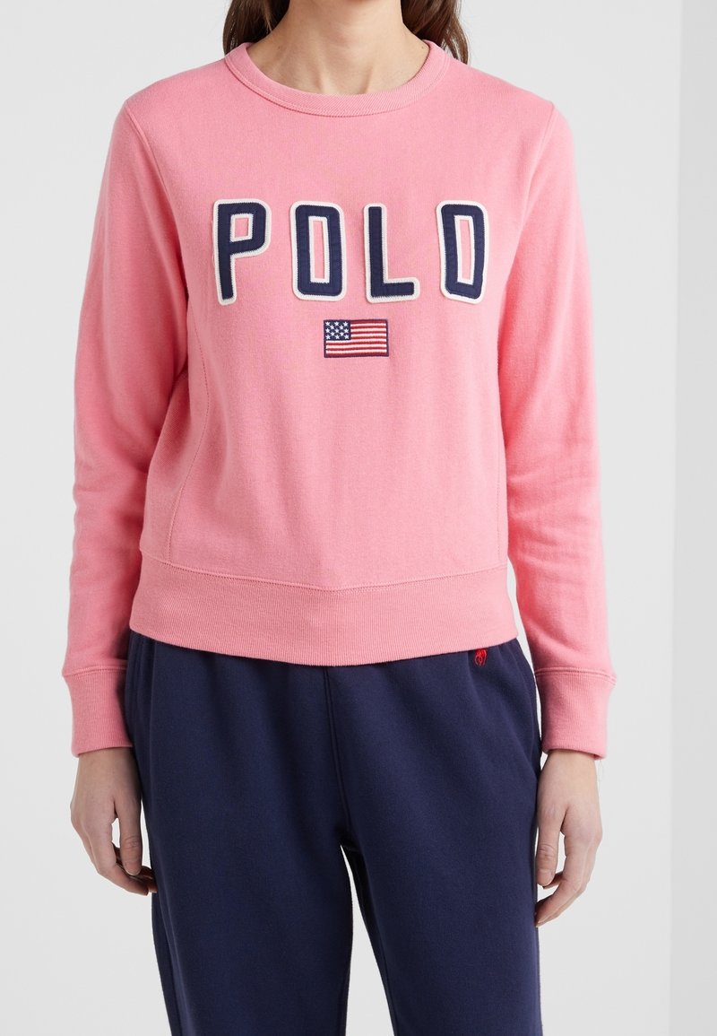 Rosa sweatshirt med broderad "POLO"-text och en amerikansk flagga som detalj. Ribbad rund hals och ärmslut, med en avslappnad passform.