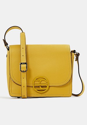 Gele leren crossbodytas met verstelbare riem en ronde metalen logo-embleem op het voorklep, afgebeeld tegen een effen lichte achtergrond.