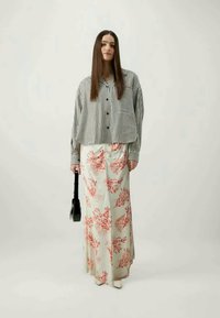 Fekete-fehér csíkos, bő szabású, gombos ing, virágmintás krémszínű maxi szoknya és fekete kézitáska. A lábbeli nem látható.