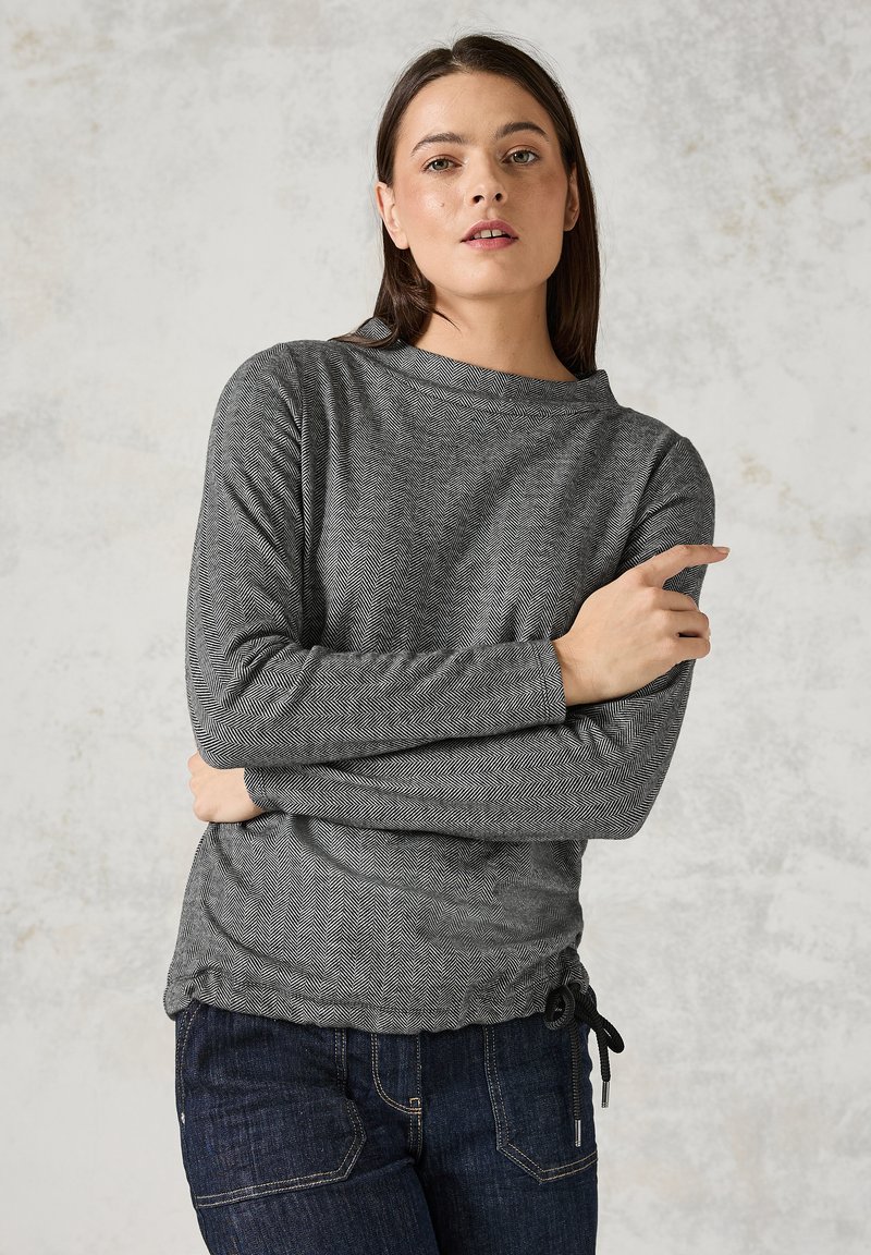 Grå långärmad topp med fiskbensmönster, rund halsringning och knyt detaljer i midjan. Matchad med mörkblå jeans.